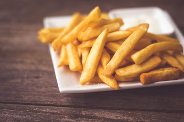 French fries fast food,french fries amount many pieces and mayonnaise, in dish square white all place on wooden table.