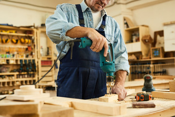 Mid section portrait of mature carpenter drilling wood while working in joinery, copy space