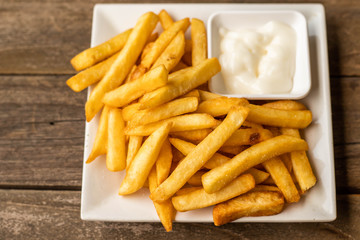 French fries fast food,french fries amount many pieces and mayonnaise, in dish square white all place on wooden table.