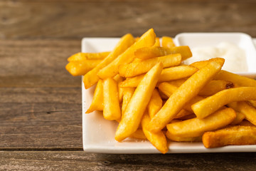 French fries fast food,french fries amount many pieces and mayonnaise, in dish square white all place on wooden table.