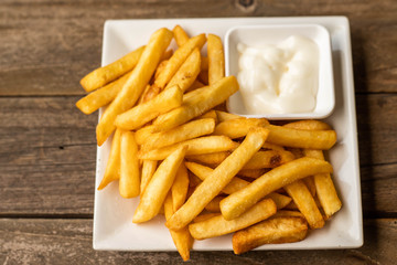 French fries fast food,french fries amount many pieces and mayonnaise, in dish square white all place on wooden table.