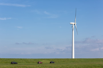 Dutch wind turbine near dike with parked cars