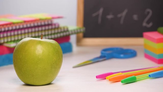 Shot of a school desk with different colorful supplies, apple and chalkboard. Back to school concept. Sliding focus. 4k.