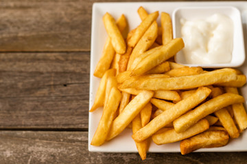 French fries fast food,french fries amount many pieces and mayonnaise, in dish square white all place on wooden table.