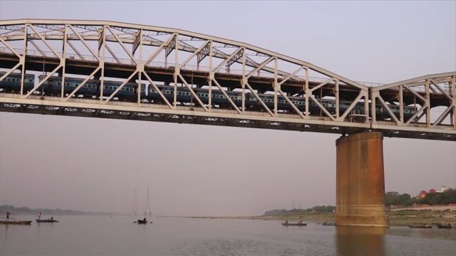 Wide low-angle dolly shot of a train passing through the long and famous Raj ghat Bridge, Ganga River, Varanasi, India