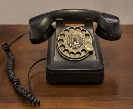 A vintage dark brown rotary dial telephone placed on an old wooden table.