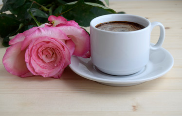 Obraz na płótnie Canvas The cup of coffee. Pink rose flower. The flower and cup of coffee are on a wooden surface.