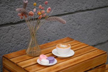 cup of coffee with flowers on wooden background and macaroons