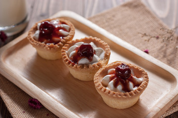 Delicious homemade mini cherry tarts and custard on wooden cutting board