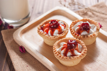 Delicious homemade mini cherry tarts and custard on wooden cutting board