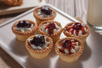 Delicious homemade mini berry tarts and custard on wooden cutting board