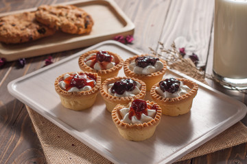 Delicious homemade mini berry tarts and custard on wooden cutting board