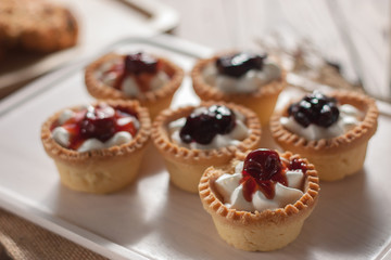 Delicious homemade mini berry tarts and custard on wooden cutting board