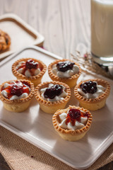Delicious homemade mini berry tarts and custard on wooden cutting board