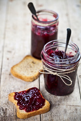 Toasted cereal bread slices and jars with homemade wild berries  and cherry jam and spoons closeup on rustic wooden table background