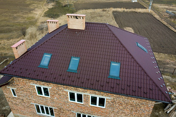 Aerial top view of building steep brown shingle roof, brick chimneys and small attic windows on...