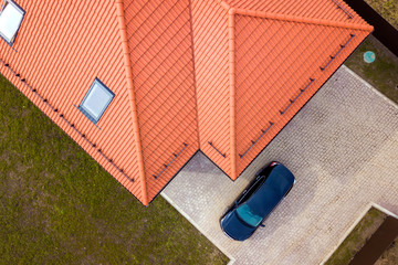 Aerial top view of house metal shingle roof with attic windows and black car on paved yard.