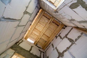 Close-up detail of house room interior under construction and renovation. Energy saving walls of hollow foam insulation blocks, wooden ceiling beams for roof frame.