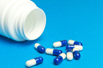 capsules ,pills  were poured from a white bottle on a blue background. Medical background, template.