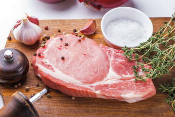 Raw pork steak with a bunch of thyme, garlic, salt, pepper and onion on a wooden cutting board top view.