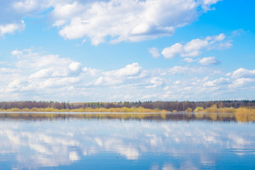 Blue sky and clouds reflected in the river. Ripples on the surface of the water. Forest on the horizon