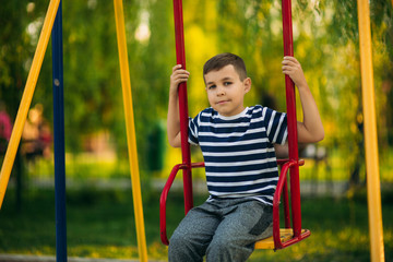 A little boy in a striped T-shirt is playing on the playground, Swing on a swing