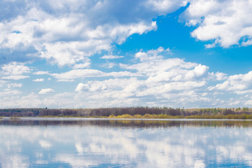 Blue sky and clouds reflected in the river. Ripples on the surface of the water. Forest on the horizon