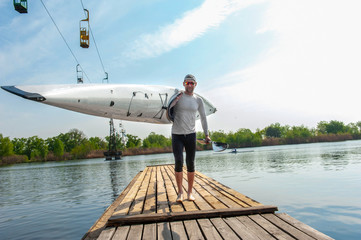 Athlete with kayak on her shoulder going on wooden dock © serguastock