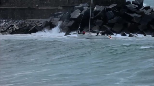 sailboat overturned by a big wave at the entrance of a port