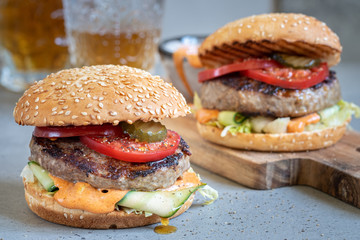 Two delicious homemade burger with beef, tomato and cucumber on a wooden cutting board