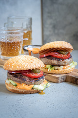 Two delicious homemade burger with beef, tomato and cucumber on a wooden cutting board