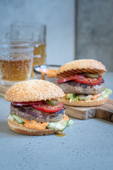 Two delicious homemade burger with beef, tomato and cucumber on a wooden cutting board