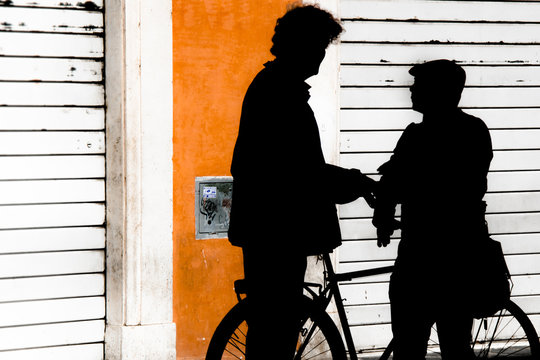 Two men with bicycles are talking in backlight near a colored wall
