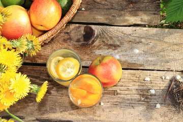 Summer drinks in the garden on an old table with dandelions. Apple and lemon juices on an old wooden background, a basket with apples and dandelions
