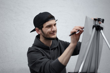 Portrait of concentrated young man painting with pencil on easel