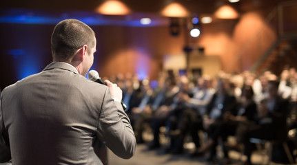 Speaker giving a talk on corporate business conference. Unrecognizable people in audience at...