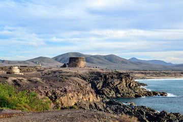 Fototapeta na wymiar Beautiful, wild shore of Fuerteventura island. Defense Toston tower/castle located in costal town of El Cotillo. Canary Islands. Spain