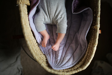 newborn Baby in wicker crib on rug leaf on dark