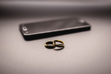 Concept of infidelity or virtual betrayal through the smartphone. golden wedding rings on a mobile phone.