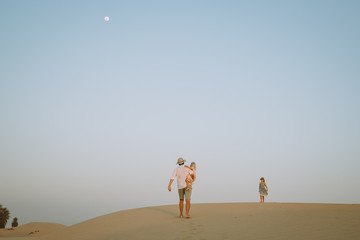 Father with two daughter standing on a sand dune in the desert with a moon on the beackground