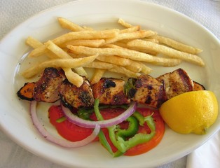 Chicken souvlaki with french fries and vegetables. White plate. Delicious greek traditional food. 