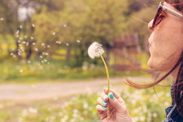 Pretty girl blowing dandelion in summer park. Green grass beautiful nature.