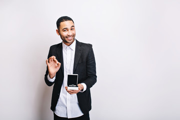 Happy handsome guy in luxury white shirt, black jacket holding gift and smiling to camera on white background. Holidays time, making surprise, ornamentation, cheerful mood