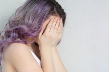 Disturbed crying young girl covering her face with hands. Space for text