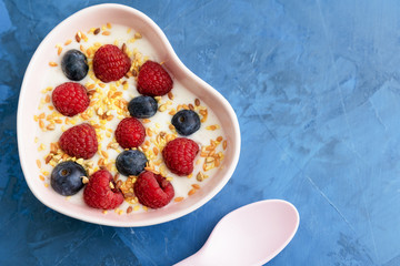 Handmade Diet Bio Yoghurt with Berries Top View. Creamy Vegetarian Food with Grains of Seed, Raspberry and Blackberry in Form of Heart Pot Plate and Modern Ceramic Spoon on Blue Table Copy Space