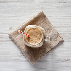 Homemade smoothie with bananas, kiwi, apples and chia seeds in a glass jar over white wooden background, top view. Close-up.