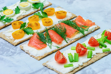 Light summer snack. Small sandwiches with different fillings. Tomatoes, herbs and red fish. Delicious bread with soft cheese. Light photo.