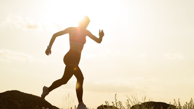 Young Beautiful Woman Running On The Mountain Trail At Hot Summer Sunset. Sport And Active Lifestyle.