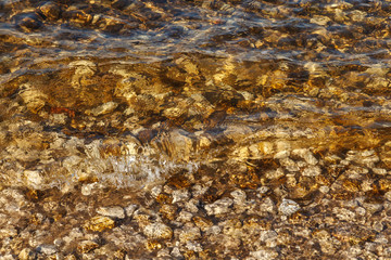 Clean water of river waves near the shore with a rocky bottom. Abstract background textures, rocks and sand in the river