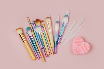 Various makeup brushes with Brush Cleansing Pad and brush guard on a pastel pink background. Flat lay, top view